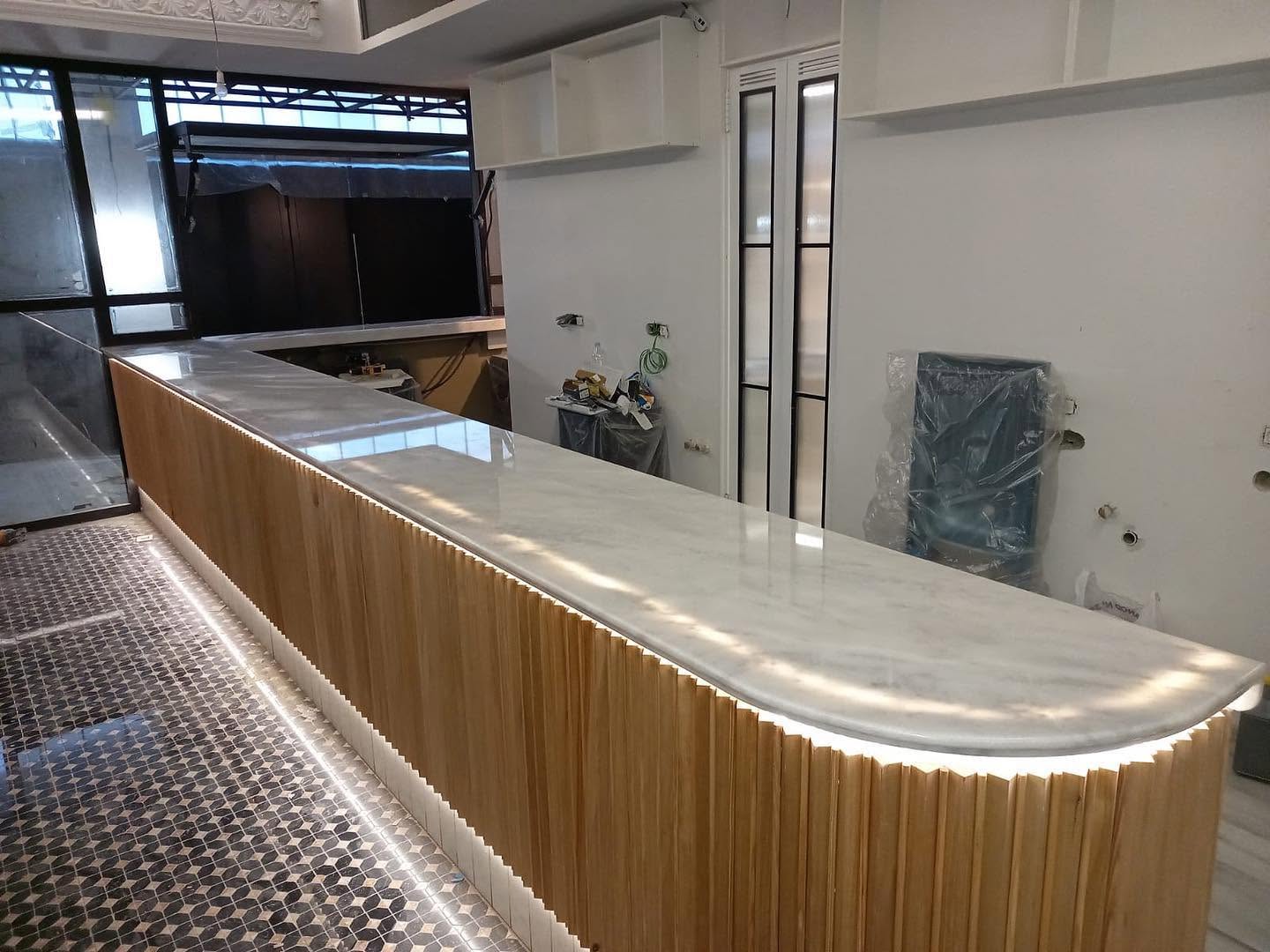 Barra de bar de mármol blanco con iluminación LED y revestimiento de madera instalada a medida por Mármoles Isidro.